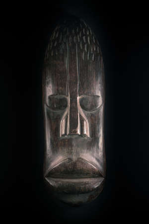 Wooden sculpture of human face in African style. Dark wood carving. African tribal mask isolated on black background. Art and culture of African people. Black history.の写真素材