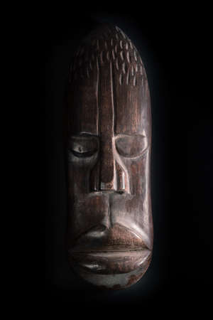 Wooden sculpture of human face in African style. Dark wood carving. African tribal mask isolated on black background. Art and culture of African people. Black history.の写真素材