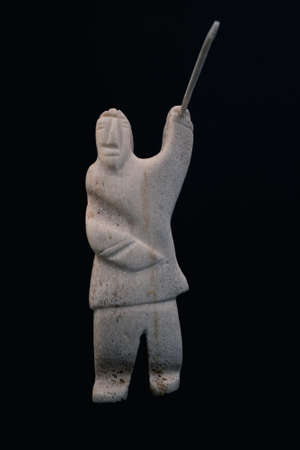 Small statue of Inuit hunter with a spear made of animal bone. Isolated on black background. Inuit art. Tribal culture of the natives in the far north. Made in Baffin Island, Nunavut, Canada.の写真素材