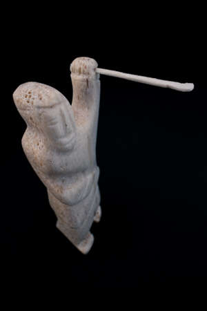 Small statue of Inuit hunter with a spear made of animal bone. Isolated on black background. Inuit art. Tribal culture of the natives in the far north. Made in Baffin Island, Nunavut, Canada.の写真素材