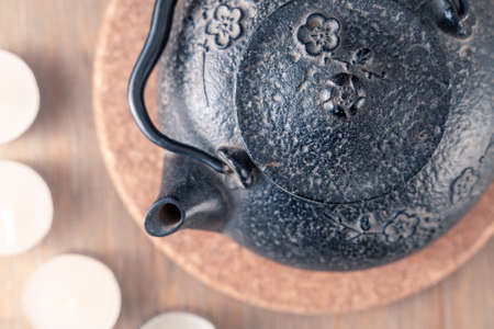 Black metal Japanese tea pot on a wooden table with tea candles and wooden box of fragrant sticks....