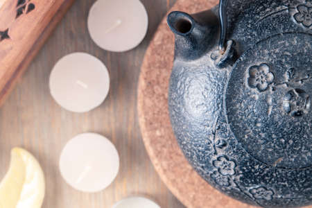 Black metal Japanese tea pot on a wooden table with tea candles and wooden box of fragrant sticks. Zen -style still life in warm, peaceful colors. Hot tea for moment of meditation.の写真素材