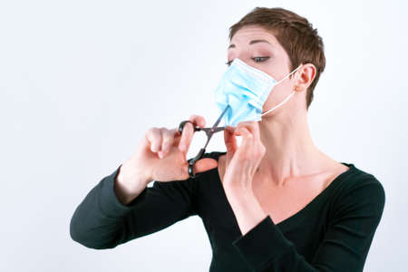 Beautiful woman with short hair removing her face mask with scissors. Life in quarantine. Dealing with coronavirus restrictions. Life during pandemic. Ending the lockdown. Easing COVID measures.の写真素材