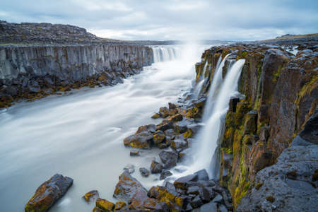 Long exposure of Selfoss waterfall in Iceland on a cloudy, rainy day. Wild river runs between steep...