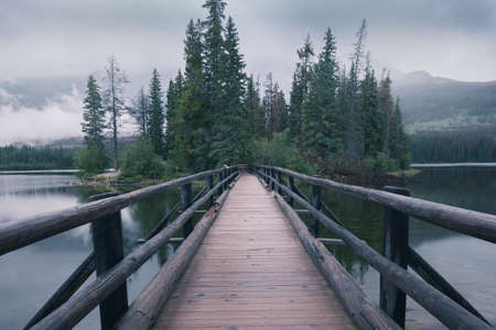 Wooden bridge leading to a small island in the background. Pyramid Lake in Canadian Rockies. Misty, moody, rainy evening in Jasper National Park, Alberta, Canada.の写真素材