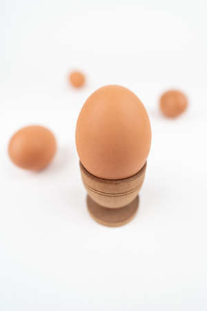 Wide angle vertical shot of hen egg in old wooden egg stand isolated on white background with three more eggs in the back. Conceptual art for egg-related foods. Breakfast minimalistic conceptの写真素材