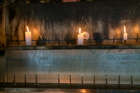 Three candles burning on a metal stand in ancient Buddhist templeの写真素材