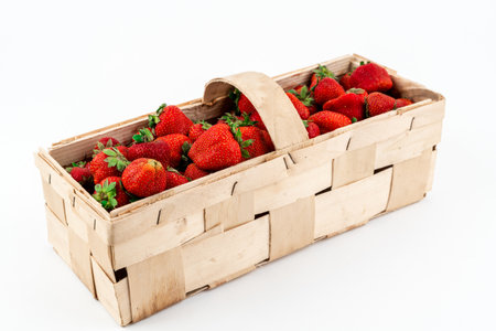 Wide angle shot of a wooden box full of red ripe strawberries isolated on white background. Harvesting summer fruitsの写真素材