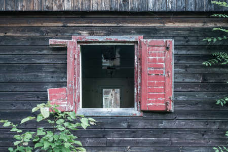 Detail of a broken window of old abandoned wooden house. Red window shutters are open and falling apartの写真素材