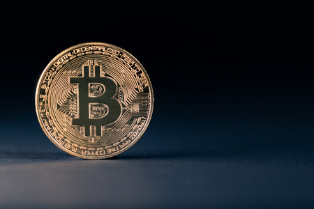 Closeup of a golden bitcoin staying on its edge illuminated from one side with very dark backgroundの写真素材