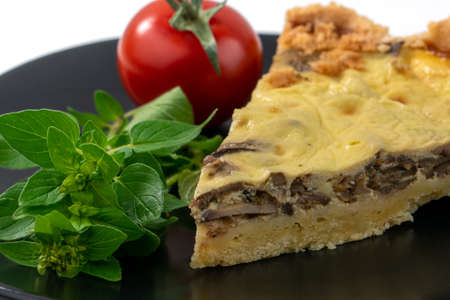 Closeup wide studio shot of a slice of yellow French salty cake, or quiche, with mushrooms on a black design plate, isolated on white background. Cherry tomatoes, green mintの写真素材