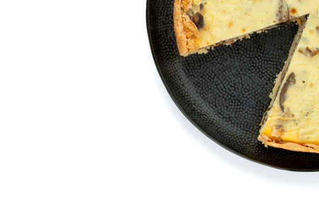 Top view studio shot of freshly baked yellow French salty cake, or quiche, with mushrooms on a black...