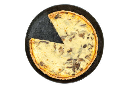 Top view studio shot of freshly baked yellow French salty cake, or quiche, with mushrooms on a black design plate, isolated on white background. One slice removed.の写真素材
