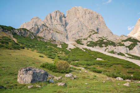 Late afternoon under rocky cliff in Austrian Alps with Alpine meadow below.の写真素材