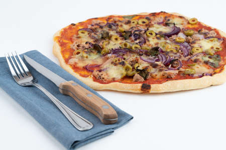 High angle studio shot of freshly baked pizza al tonno isolated on white background. Tuna, olives, onions, veggies, crust, tomato sauce. Still life with blue cloth and cutlery set.の写真素材