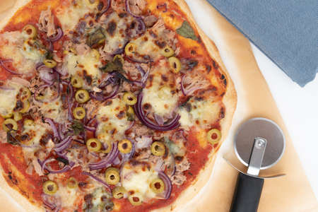 Top view studio shot of freshly baked pizza al tonno on baking paper, isolated on white background. Blue cloth and pizza slicer.の写真素材