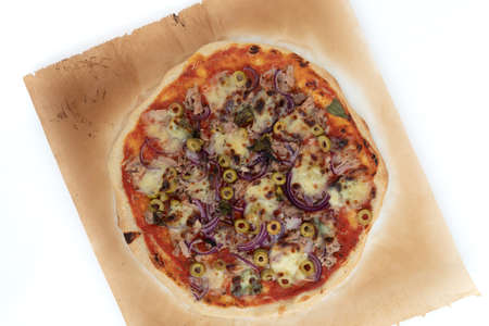 Top view studio shot of freshly baked pizza al tonno on baking paper, isolated on white background. Olives, tuna, onion, veggies, crust.の写真素材