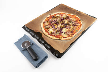 High angle studio shot of homemade pizza al tonno on black baking tray and baking paper, isolated on white background. Blue cloth and pizza slicer.の写真素材