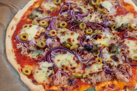 High angle view detail closeup studio shot of freshly baked pizza al tonno on baking paper. Olives, tuna, onion, veggies, crust.の写真素材