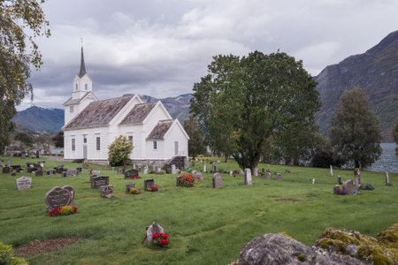 Traditional white wooden Christian church in Scandinavian style with graveyard around it. Cloudy day in Norwegian countryside.の写真素材