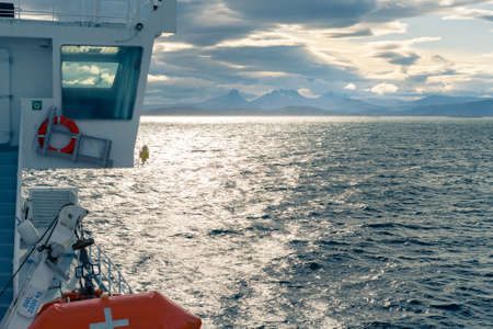 Cabin of a boat sailing in the sea by Lofoten Islands. Dramatic clouds and mountain range on the distant horizon. Harsh weather of arctic summer and wild Norwegian northern nature.の写真素材