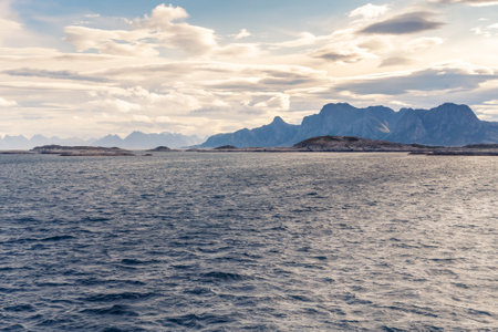 Stormclouds with sun shining through them above dramatic mountain range of Lofoten Islands, viewed from boat on the sea between Bodo and Moskenes. Dramatic landscape of Norwegian arctic.の写真素材