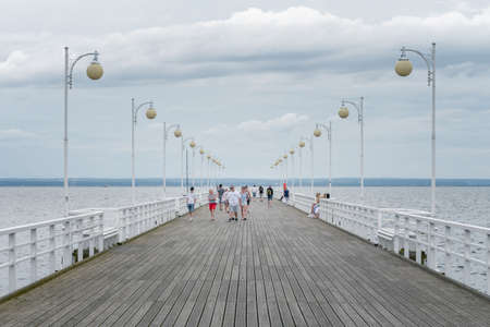 Jurata, Poland - 08.01.2021: People walking on Ocean pier of Jurata on a cloudy summer day on a Baltic Coast. Wooden wallk and vintage sreet lamps.のeditorial素材
