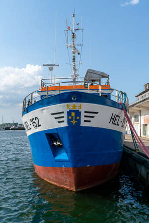 Hel, Poland - 08.02.2021: Front closeup shot of blue fishing boat with coat of arms of Hel on it, docked at concrete pier, on a sunny summer day.のeditorial素材