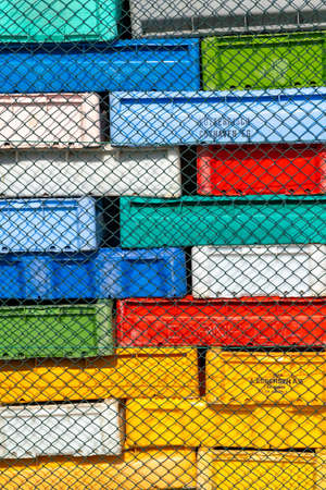 Hel, Poland - 08.02.2021: Lot of colorful plastic boxes, usually used to store fish, mounted in big blocks behind a steel fence in port of Hel. Interesting pattern or texture.のeditorial素材