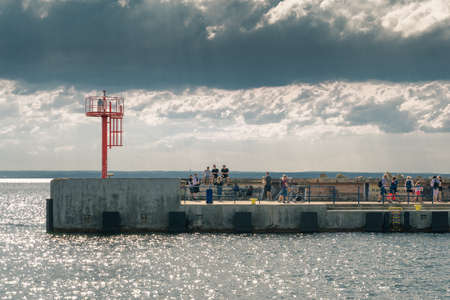 Hel, Poland - 08.02.2021: People walking and sitting along concrete ocean pier on a partly cloudy summer day with dramatic sky in the background. Leisure time in the harbour.のeditorial素材
