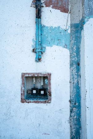 Detail vertical shot of old electric wires leading into a box with vintage electric switches on a white, blue and red cracked wall. Abandoned place concept.の写真素材