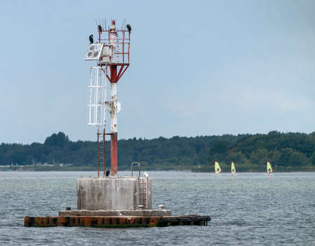Group of Great cormorants, Phalacrocorax carbo, sitting on atop of metal red and white radio tower or beacon in Baltic sea near Jastarnia, Poland. Baltic wildlife and naval technology.の写真素材