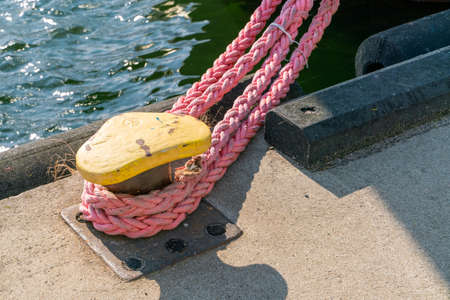 Detail closeup shot of yellow steel harbour knob with a strong pink rope attached to it, securing a moored boat.の写真素材