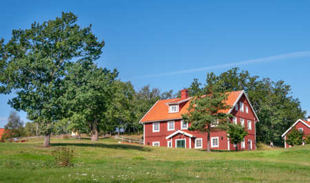 Vastervik, Sweden - 08.23.2021: Typical red wooden countryside house in nature of southern Sweden on a beautiful sunny summer day. Relaxing rural landscape.のeditorial素材