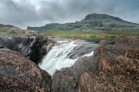 Closeup, wide, low angle shot of mighty Stuor Muorkkegarttje waterfall on Lulealven river on a partly cloudy day of arctic summer. Stora Sjofallet national park, Sweden.の写真素材