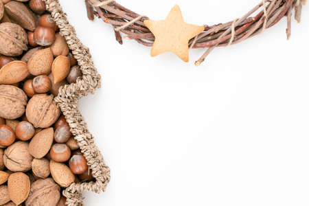 Top studio shot of basket full of mixed nuts and dry handmade Christmas wreath with star gingerbread, isolated on white background. Christmas concept. Traditional hand work.の写真素材