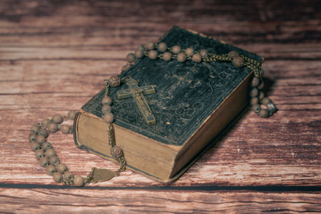 Wide studio shot of very old, vintage Holy Bible with lots of ornaments on the cover and yellow pages and old rosary on vintage wooden desk Christianity concept. Time of prayer.の写真素材