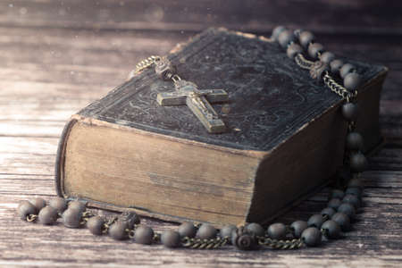 Detail studio shot of very old, vintage Holy Bible with lots of ornaments on the cover and yellow pages and old rosary on vintage wooden desk Christianity concept. Time of prayer.の写真素材