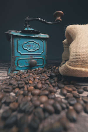 Vertical low angle studio shot of still life with vintage manual green metal coffee grinder, jute bag and coffee beans on old wooden table. Coffee concept.の写真素材