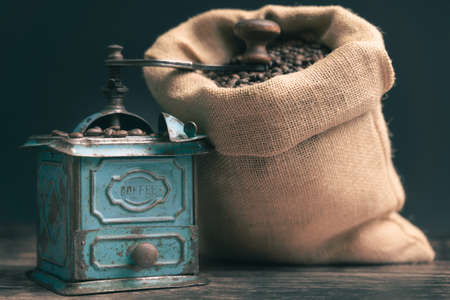 Horizontal detail straight studio shot of still life with vintage manual green metal coffee grinder, jute bag and coffee beans on old wooden table. Coffee concept.の写真素材