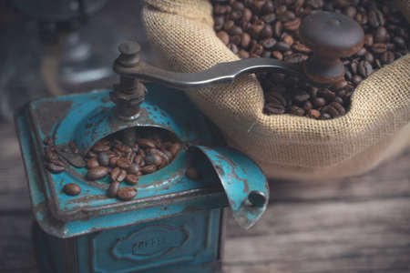 Horizontal detail high angle studio shot of still life with vintage manual green metal coffee grinder, jute bag and coffee beans on old wooden table. Coffee concept.の写真素材