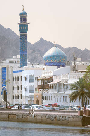 Muscat, Oman - 04.04.2018: Vertical shot of a blue mosque in the bay of old town of Muscat, Oman on a hot day. Blue mosque and minaret, white buildings and sandstone rock in the hazy background.のeditorial素材