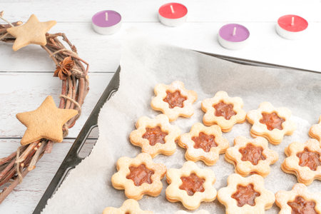 High angle studio shot of still life with traditional Christmas sweets, line dough with apricot ham, powdered with sugar, on white baking paper. Wreath and candles. Christmas theme concept.の写真素材