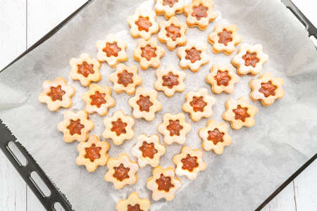Top studio shot of traditional Christmas sweets, line dough with apricot ham, powdered with sugar, on white baking paper and black baking tray on a white wooden table. Christmas theme background.の写真素材