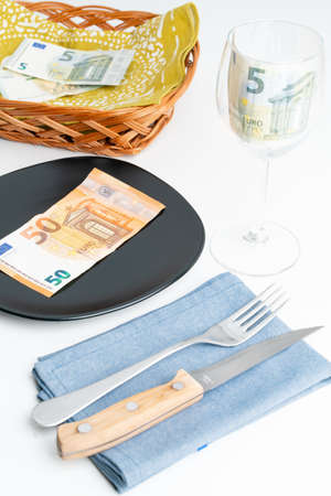 Conceptual studio shot of dinner table with euro bank notes on the plate instead of food. Concept for rising food prices, inflation, economic crisis, consumer prices index.の写真素材