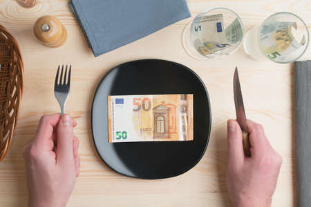 Conceptual studio shot of dinner table with euro bank notes on the plate instead of food. Concept for rising food prices, inflation, economic crisis, consumer prices index.の写真素材