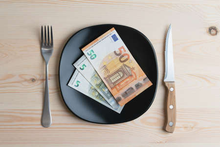 Conceptual studio shot of dinner table with euro bank notes on the plate instead of food. Concept for rising food prices, inflation, economic crisis, consumer prices index.の写真素材