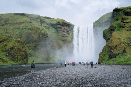 Skogafoss, Iceland - 06.19.2017: People walking around the Skogafoss waterfall in southern Iceland on a cold cloudy day of Icelandic summer.のeditorial素材