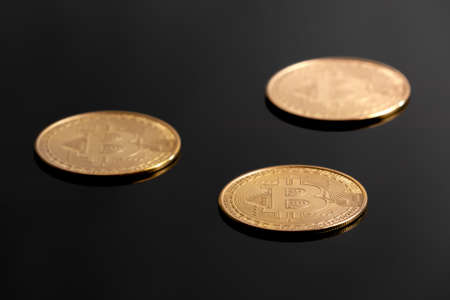 Detail studio shot of three golden bitcoins laying on black reflective surface. Concept for electronic money, crypto currency, blockchain investment, wealth, mining, financial markets.の写真素材