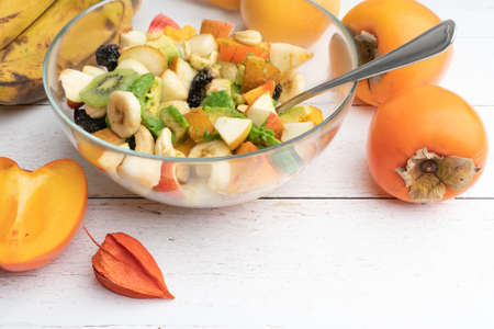Studio shot of glass bowl with freshly made fruit salad in it on a white wooden table. Healthy eating concept. Vegetarian food. Vegan raw diet. Assorted fruits mixed in a bowl.の写真素材